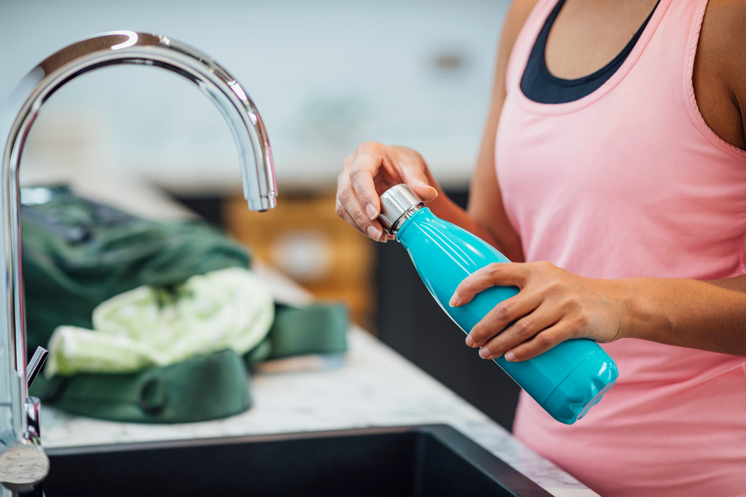An unrecognizable woman filling up a reusable water bottle at a kitchen sink.