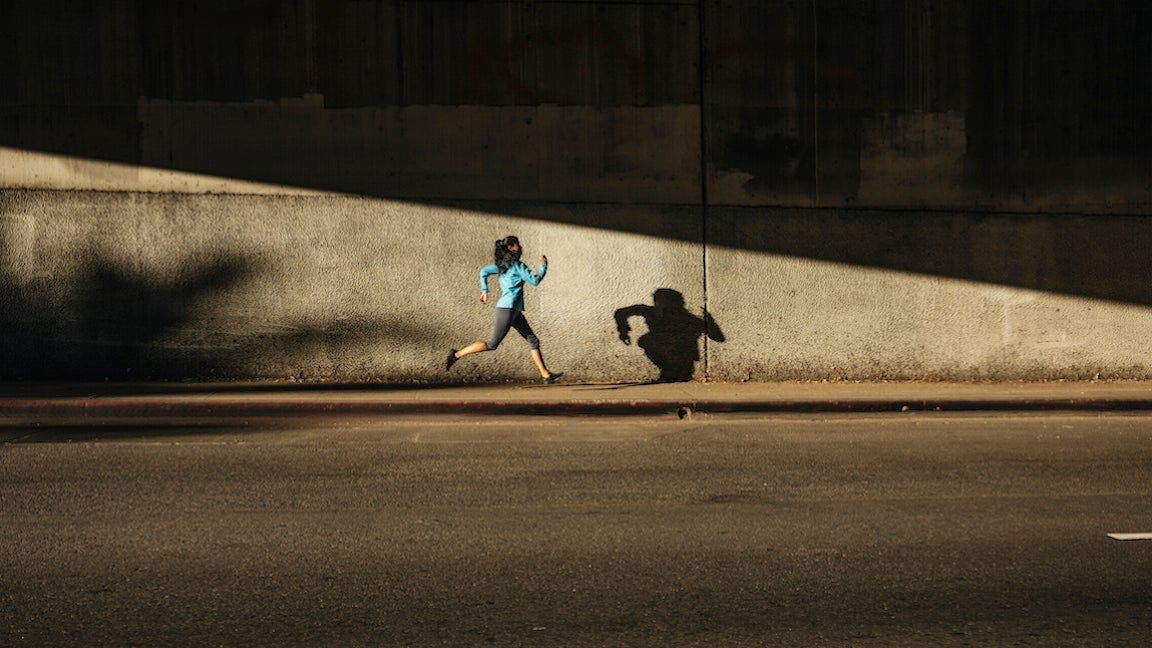 Woman running against wall on city street during a tempo run.