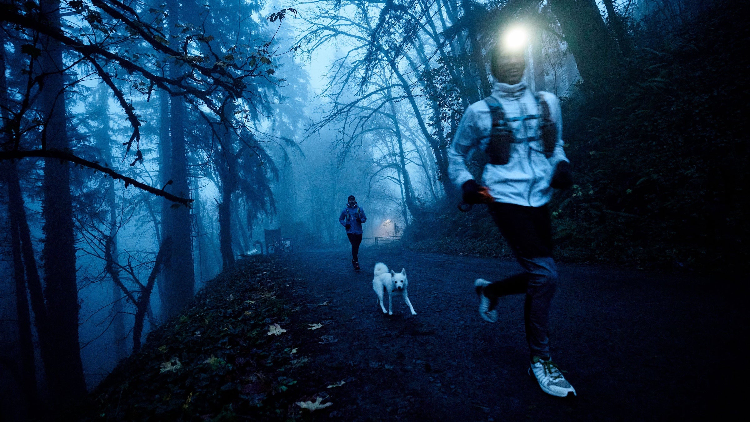 A man in white runs through a dark blue forest