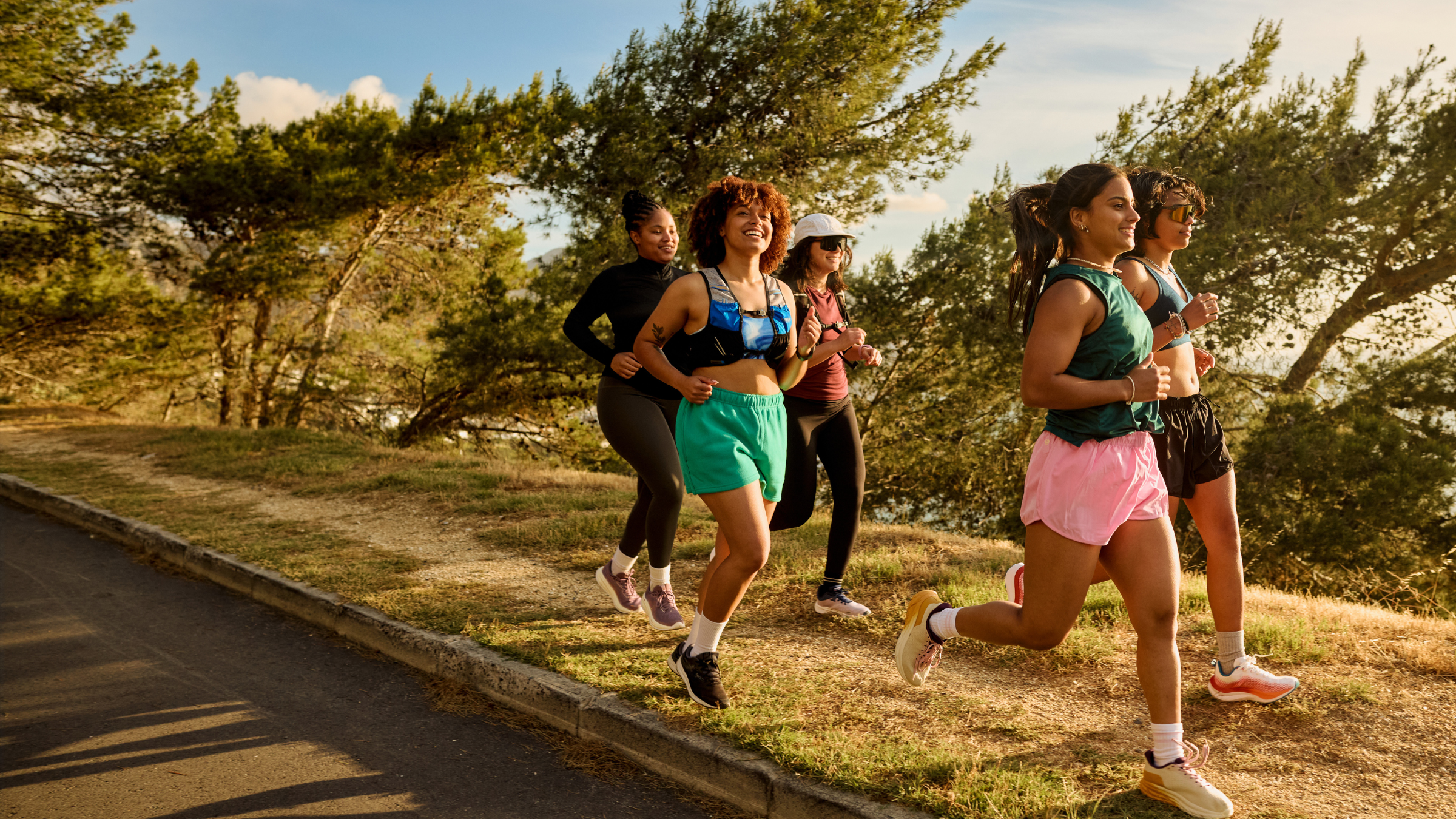 women running down a hill with windblown trees in the background on a sunny day